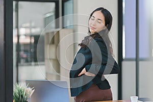 A businesswoman stretches lazily on her desk for relaxation while working in the office.