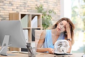 Businesswoman suffering from heat in front of small fan