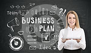 Businesswoman with a tablet near business plan icons on blackboard