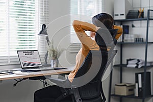 Businesswoman taking a break to stretch with a red graph trending downwards in home office.