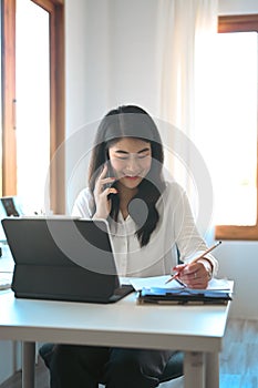 Businesswoman taking on mobile phone and making notes on notebook.