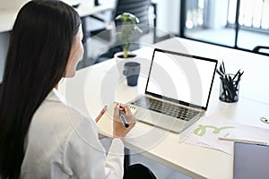 A businesswoman taking notes on her notebook while looking at her laptop screen