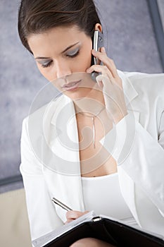 Businesswoman taking notes and making phone call