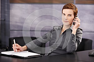 Businesswoman taking notes while on phone call