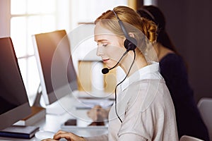 Businesswoman talking by headset in office. Call center and diverse people group in business