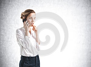 Businesswoman talking with phone in hand, mockup empty wall