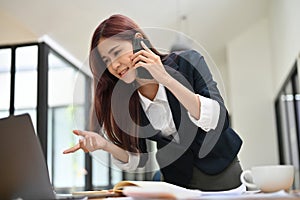 Businesswoman talking on the phone with her supplier and looking the detail on laptop screen