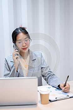 A businesswoman is talking on the phone, taking notes, and reading information on her laptop