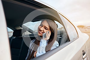 Businesswoman talking on phone while travelling in a taxi. Woman sitting on back seat of car using laptop and phone.