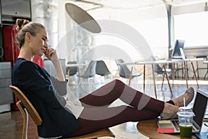 Businesswoman talking on smart phone while relaxing on chair at office