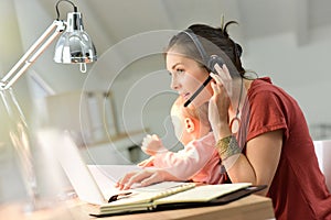 Businesswoman teleworking on laptop holding her baby