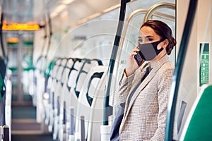 Businesswoman In Train Carriage Talking On Mobile Phone Wearing PPE Face Masks During Pandemic