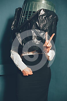 Businesswoman with trash can on her head showing V sign or victory gesture with hand. Crisis concept. Tinted image