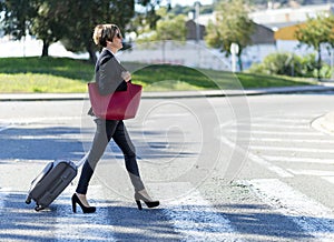 Businesswoman with trolley bag walking in urban environment. Wearing a red bag