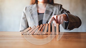 A businesswoman try to use finger to stop falling wooden dominoes blocks for business solution concept