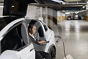 Businesswoman typing on gadget during EV refuel in parking