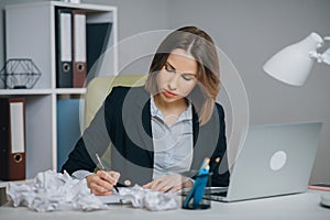 Businesswoman typing his piece of art, crumpling and wasting a sheet of paper dissatisfied with result. Crumpled pieces