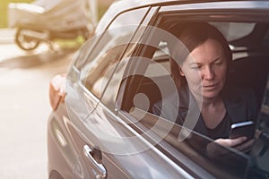 Businesswoman typing message on mobile phone inside of company car