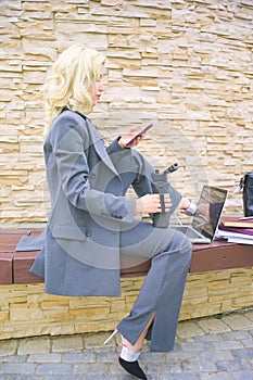 A businesswoman is typing a text message on her phone. Woman sitting on a bench