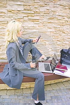 A businesswoman is typing a text message on her phone. Woman sitting on a bench