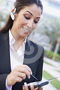 Businesswoman using bluetooth earpiece and PDA