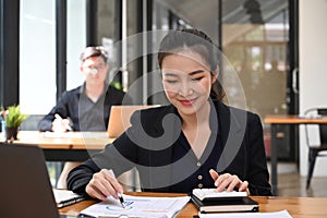 Businesswoman using calculator and checking financial reports.