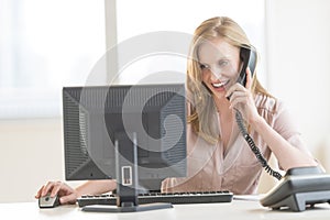 Businesswoman Using Computer While Conversing On Landline Phone