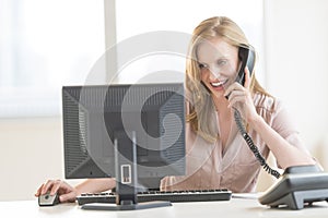 Businesswoman Using Computer While Conversing On Landline Phone photo