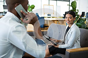 Businesswoman using digital tablet while a colleague talking on mobile phone