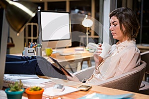 Businesswoman using digital tablet and holding coffee cup at her desk