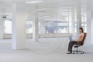 Businesswoman Using Laptop On Chair In Empty Office