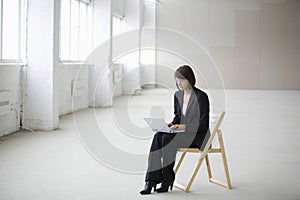 Businesswoman Using Laptop While Sitting On Chair In Warehouse