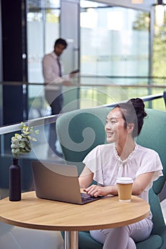 Businesswoman Using Laptop Working At Table In Breakout Seating Area Of Office Building 