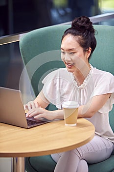 Businesswoman Using Laptop Working At Table In Breakout Seating Area Of Office Building 