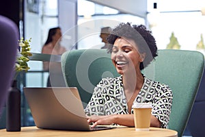 Businesswoman Using Laptop Working At Table In Breakout Seating Area Of Office Building 