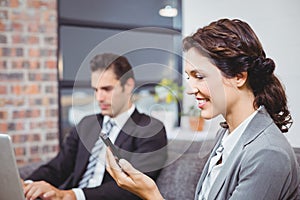 Businesswoman using mobile phone while colleague working