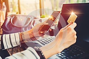 Businesswoman using mobile phone making credit card online payment on her phone app with laptop computer background