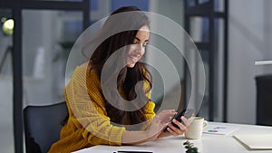Businesswoman using mobile phone at workplace. Smiling woman browsing internet