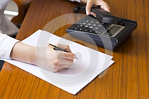 Businesswoman using phone, taking notes at office desk