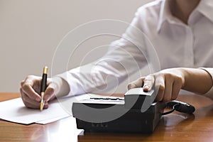 Businesswoman using phone, taking notes at office desk