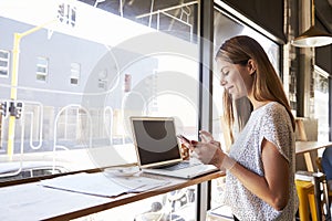 Businesswoman Using Phone Whilst Working In Coffee Shop