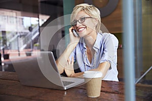 Businesswoman Using Phone Working On Laptop In Coffee Shop