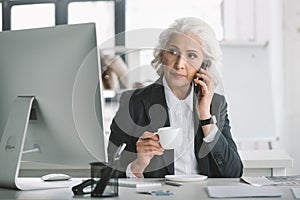 Businesswoman using smartphone and drinking coffee at workplace in office