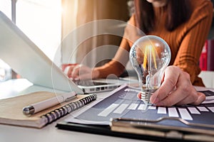 Businesswoman using tabtop computer and holding light bulb, with idea.