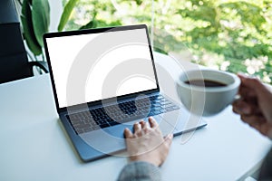 A businesswoman using and touching on laptop touchpad with blank white desktop screen while drinking coffee in