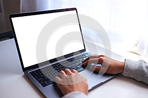 a businesswoman using and typing on laptop computer keyboard with blank white desktop screen on the table