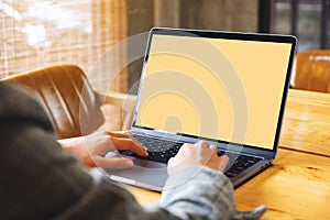 A businesswoman using and typing on laptop computer keyboard with blank white desktop screen on wooden table