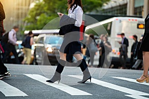 Businesswoman walking on crosswalk and texting on smartphone in city street