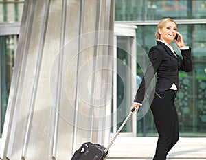 Businesswoman walking with suitcase and talking on mobile phone