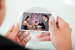 Businesswoman watching couple toasting wineglasses on cellphone